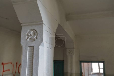 Foto de Antiguos símbolos comunistas - martillo y hoz - de la antigua Yugoslavia grabados en las columnas de un pasillo, abandonaron la escuela primaria desde 1948 d.C. con paredes llenas de graffiti. Vevcani-Macedonia del Norte. - Imagen libre de derechos