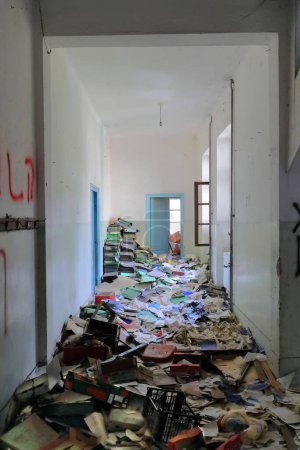 Old corridor inside the remains of a ruined, abandoned former primary school built in AD 1948 full of rubble, rubbish, stacked ring binder folder, graffiti and peeling walls. Vevcani-North Macedonia.
