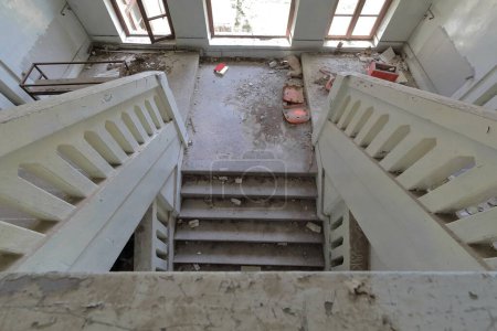 Two flight of stairs with intermediate half landing inside the remains of a ruined, abandoned former primary school building from AD 1948, full of rubble with peeling walls. Vevcani-North Macedonia.