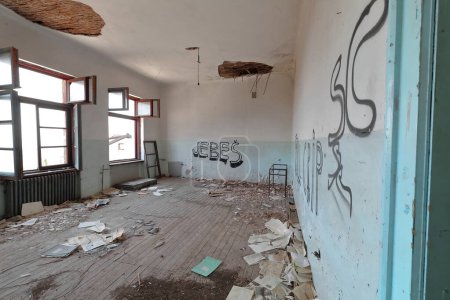 Foto de Antiguo aula dentro de los restos de una antigua escuela primaria en ruinas, abandonada, construida en 1948 d.C. llena de escombros con ventanas rotas, graffiti y paredes y techos pelados. Vevcani-Macedonia del Norte. - Imagen libre de derechos