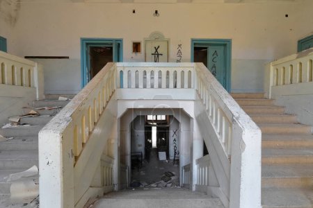 Zwei Treppen mit mittlerer Halbtreppe in den Überresten eines verfallenen, verlassenen ehemaligen Grundschulgebäudes aus dem Jahr 1948, voller Schutt mit abblätternden Wänden. Vevcani-Nordmakedonien.