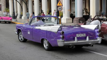 Foto de La Habana, Cuba-07 de octubre de 2019: Coche clásico americano de color púrpura y blanco, tanque de yanqui Dodge Custom Royal Lancer Convertible de 4 puertas desde 1957 conduce hacia el sur a lo largo del Paseo del Prado. - Imagen libre de derechos