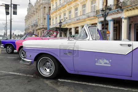 Foto de Havana, Cuba-October 07, 2019: Purplish blue-pink-lilac classic convertible cars - Dodge Custom Royal Lancer '57, Chevrolet Styleline DeLuxe' 52, Ford Fairline Sunliner '57- parada en Paseo del Prado. - Imagen libre de derechos