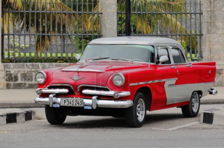 Foto de Havana, Cuba-October 7, 2019: Red-gray old American classic car -almendron, yank tank- Dodge Kingsway Custom 4 door Sedan of 1956 (1955 model's frontal grille) parks on Avenida del Puerto-Port Avenue. - Imagen libre de derechos