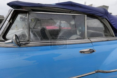 Foto de La Habana, Cuba-7 de octubre de 2019: Detalle de una ventana y capucha para automóvil convertible clásico estadounidense Chevrolet Styleline DeLuxe 1950 azul estacionado bajo la lluvia en la Plaza de la Revolución. - Imagen libre de derechos