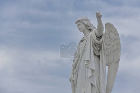 Estatua de ángel masculino de mármol blanco sobre un pedestal con el brazo izquierdo levantado, Cementerio de Colón Cementerio conocido por sus numerosos monumentos elaboradamente esculpidos, estimados en más de 500 mausoleos. La Habana-Cuba.