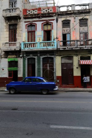 Foto de La Habana, Cuba-8 de octubre de 2019: El viejo auto clásico americano azul oscuro almendro, tanque de yanqui Buick Special DeLuxe Sedan de 4 puertas 1952 conduce por San Lazaro St más allá de una fila de casas de estilo ecléctico de principios de 1900 - Imagen libre de derechos