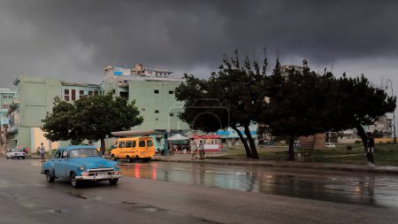 Foto de Havana, Cuba-October 8, 2019: Blue American classic car-almendron- Chevrolet Styleline DeLuxe 4-door Sedan 1950-1951 grille- conduce por la calle San Lázaro-Antonio Maceo Park después de un fuerte aguacero. - Imagen libre de derechos
