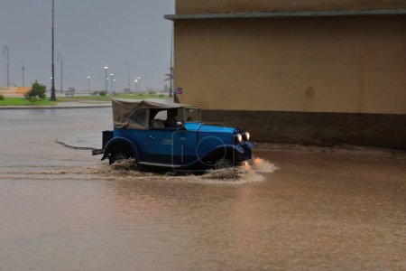 Foto de La Habana, Cuba-8 de octubre de 2019: Blue American classic car-almendron- Ford 400-A Convertible Sedan 1931 vadea a través de un charco profundo en Marina Street que viene de Malecon Promenade bajo un fuerte aguacero. - Imagen libre de derechos
