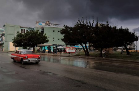 Téléchargez les photos : La Havane, Cuba-8 octobre 2019 : Vieille voiture classique américaine rouge-blanche -almendron, réservoir à yanke- Pontiac Chieftain Berline 4 portes 1957 descend la rue San Lazaro après une forte averse de pluie - en image libre de droit