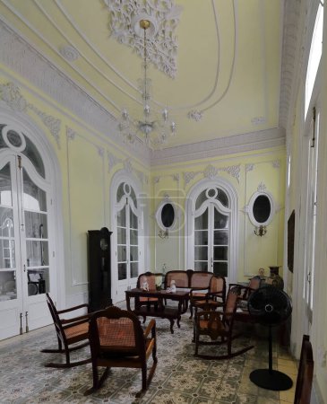 Téléchargez les photos : Cienfuegos, Cuba-11 octobre 2019 : Hall de l'ancien palais Palacio Ferrer, aujourd'hui musée Museo de Artes, affichant murs et plafond jaune pâle, moulures décoratives blanches et meubles anciens en bois. - en image libre de droit