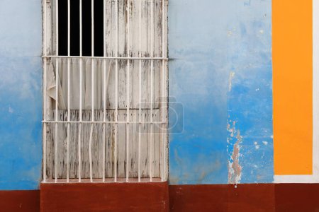 Foto de Trinidad, Cuba-12 de octubre de 2019: Dilapidada fachada de casa de estilo colonial cerca de la Plaza Mayor con la frecuente ventana local larga como puerta, pared pintada en llamativa combinación de colores. - Imagen libre de derechos