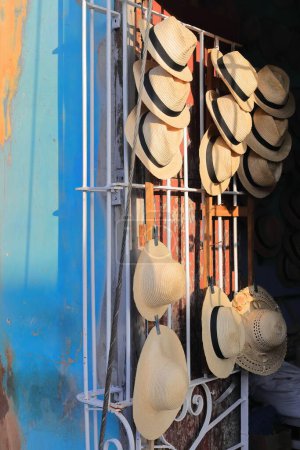 Set of straw hats -Panama, Ecuadorian, Jipijapa or Toquilla- hanging from a wooden frame attached to the open, white painted wrought-iron grille of a shop on a street of the Plaza Mayor Square area.