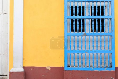 Trinidad, Kuba-12. Oktober 2019: Renovierte, aber abgeplatzte Fassade eines Hauses im Kolonialstil in der Nähe des Plaza Mayor mit dem häufigen lokalen türähnlichen Fenster, Wand in auffälliger Farbkombination gestrichen.