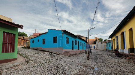 Photo for Horseman riding next to a blue-walled house on pink-painted plinth, Calle Amargura Street and Callejon de la Soledad Alley corner. Trinidad-Cuba-273 - Royalty Free Image