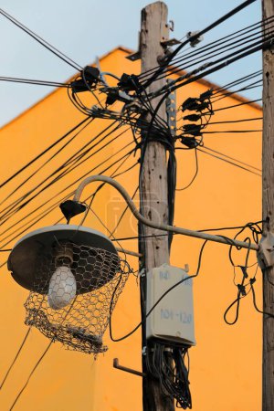 Wirrwarr von Stromkabeln an einem Lichtmast neben der pastellorangen Fassade eines Kolonialhauses an der Ostseite der Straße Calle Desengano, Hausnummer 424, in der Plaza Mayor. Trinidad-Kuba.