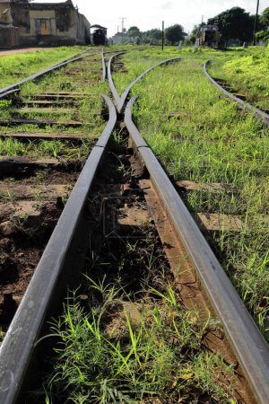Photo for Steel railway tracks at the main station anchored to a combination of concrete and wood sleepers placed upon a bed of ballast almost fully covered in grass, intersecting at a turnout. Trinidad-Cuba. - Royalty Free Image
