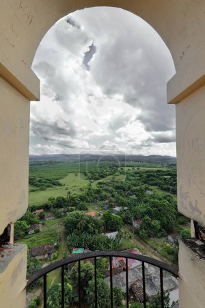 Photo for Eastward, high-angle view framed by a round arch on the uppermost level of the Manaca Iznaga tower over the estate's farmland, forests, patchwork fields and the far Escambray Mountains. Trinidad-Cuba. - Royalty Free Image