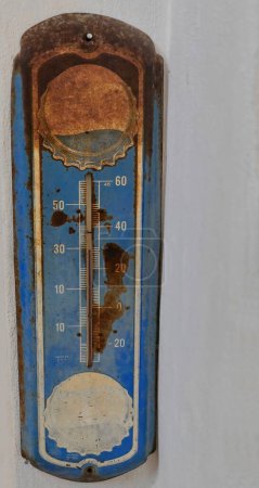 Santa Clara, Cuba-October 14, 2019: Vintage steel wall thermometer with faded illustrations of the advertised brand, rusty blue and still working -temperature correctly displayed in degrees Celsius-.