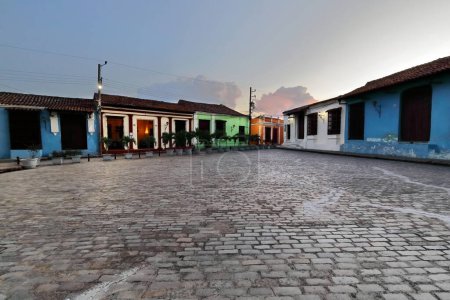 Camaguey, Cuba-15 octobre 2019 : Vue vers le sud-ouest sur la place San Juan de Dios pavée de 1732 après JC aux bâtiments coloniaux le long de la rue transversale Calle Matias Varona au crépuscule.