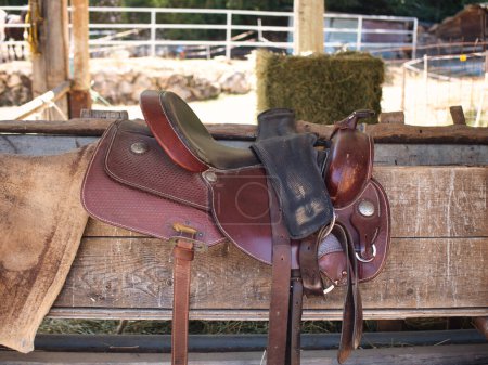 Téléchargez les photos : The saddle is brown on the fence in a shallow depth of field. leather saddle, harness for horses. Western saddles for horses on the rack, ready for dressage training. Equestrian sport background. - en image libre de droit