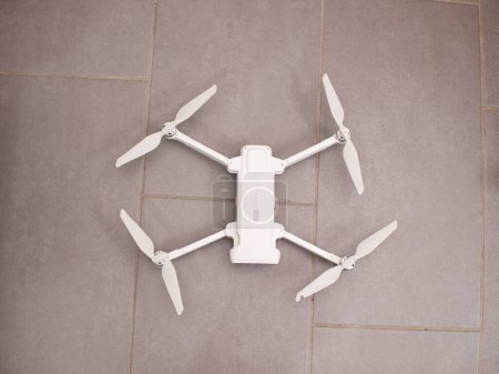 Téléchargez les photos : Un quadcopter blanc est stationné au-dessus d'un plancher de tuiles. Le drone semble stationnaire, reposant sur la surface plane des carreaux de sol - en image libre de droit
