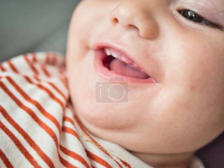 Eine Nahaufnahme, die den freudigen Gesichtsausdruck eines Babys einfängt, das lächelt und zwei kleine Zähne zeigt. Die Kinderaugen funkeln vor Freude, und es gibt einen Hauch von Verspieltheit in diesem ehrlichen Moment