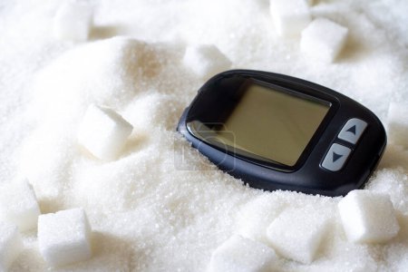 Glucometer sobre el azúcar derramado, consumo excesivo de azúcar, concepto de diabetes