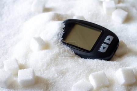 Glucometer sobre el azúcar derramado, consumo excesivo de azúcar, concepto de diabetes