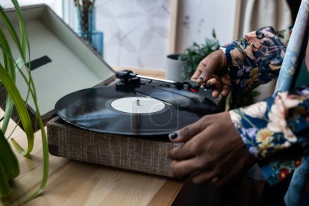 Photo for Hands of young black man with nail polish putting vinyl record on needle player standing on wooden windowsill before listening retro music - Royalty Free Image