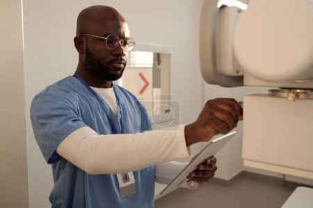 Téléchargez les photos : Young serious radiologist switching on x-ray equipment before examination of patients while standing in medical office - en image libre de droit
