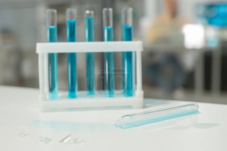 Téléchargez les photos : Shattered glass of broken test tube on desk against group of flasks with blue liquid in modern clinic or scientific laboratory - en image libre de droit