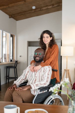 Téléchargez les photos : Happy young interracial couple in casualwear looking at camera with smiles while spending time together at home - en image libre de droit