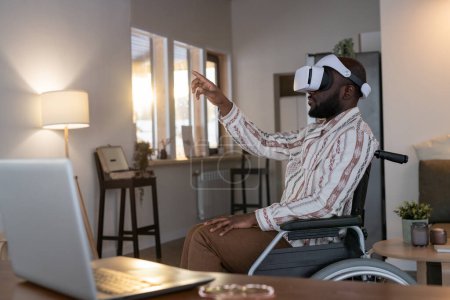 Téléchargez les photos : African American man with disability preparing virtual presentation while sitting in wheelchair by his workplace in living room at home - en image libre de droit