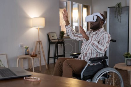 Téléchargez les photos : Contemporary software developer in vr headset touching virtual display while sitting in wheelchair and working from home - en image libre de droit