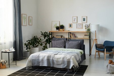 Foto de Part of spacious bedroom with double bed and shelves in the center surrounded by pictures in frames on walls and domestic plants - Imagen libre de derechos
