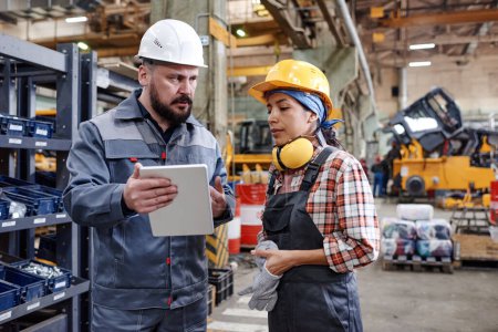 Photo for Bearded mature engineer with tablet making presentation of new technical project to young female colleague in factory - Royalty Free Image