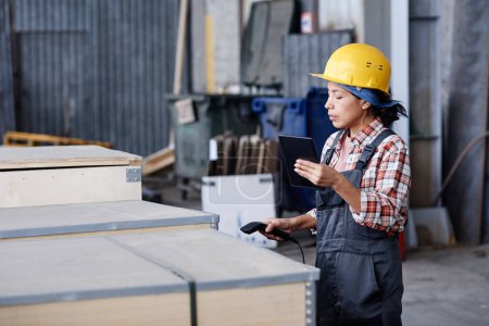 Foto de Young female worker of distribution warehouse scanning code on container with new equipment or spare parts for machines - Imagen libre de derechos