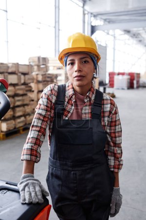 Photo for Young serious female engineer in workwear standing by cart with package in front of camera in distribution warehouse - Royalty Free Image