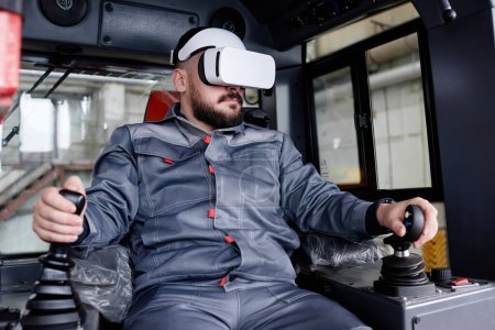Foto de Confident male builder in vr headset and workwear holding by gearshifts while sitting inside construction machine and driving it - Imagen libre de derechos