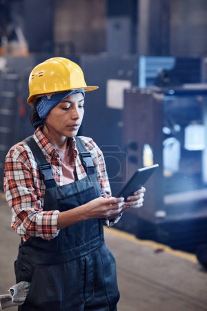Foto de Serious female worker of industrial plant using tablet for check-up of online orders while standing in distribution warehouse - Imagen libre de derechos