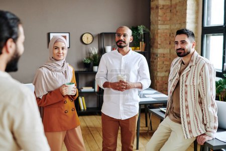 Foto de Group of coworkers looking at young Muslim businessman during discussion of new business trends or working plans - Imagen libre de derechos