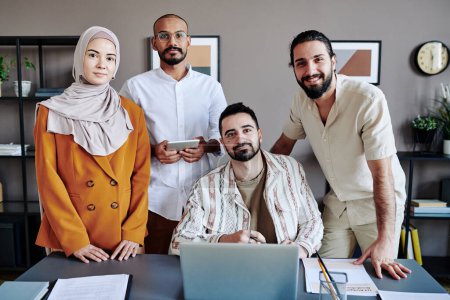 Téléchargez les photos : Four young successful Muslim office workers in casualwear looking at camera while preparing presentation for conference - en image libre de droit