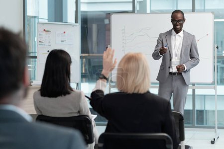 Foto de Young successful business coach in suit pointing at woman with raised hand at seminar while questioning audience after presentation - Imagen libre de derechos