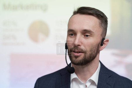 Téléchargez les photos : Young confident broker or business coach with microphone by his mouth making speech in front of audience at conference or seminar - en image libre de droit
