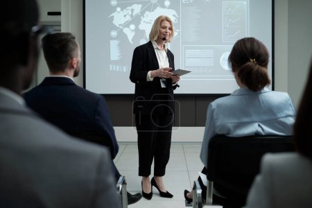 Foto de Experienced female business coach speaking in microphpne in front of audience while standing against interactive board - Imagen libre de derechos