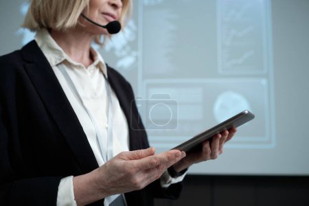 Foto de Contemporary female business coach with digital tablet making speech at conference while standing against interactive board with data - Imagen libre de derechos