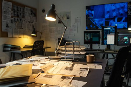 Foto de Workplace of fbi agent with lamp lighting criminal profiles and other stuff on desk on background of security camera on large screen - Imagen libre de derechos