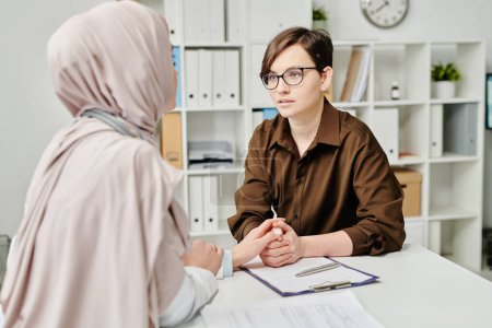 Téléchargez les photos : Jeune patiente malade regardant un médecin musulman dans le hijab lors d'une discussion sur son diagnostic et ses méthodes de traitement médical - en image libre de droit