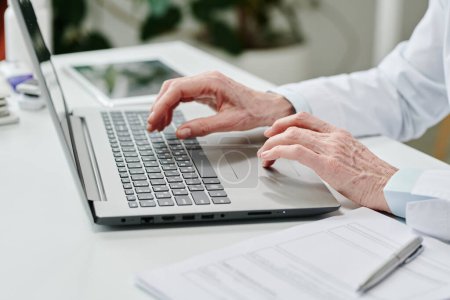 Foto de Hands of contemporary experienced online doctor over laptop keyboard during online consultation of patients and answering their questions - Imagen libre de derechos
